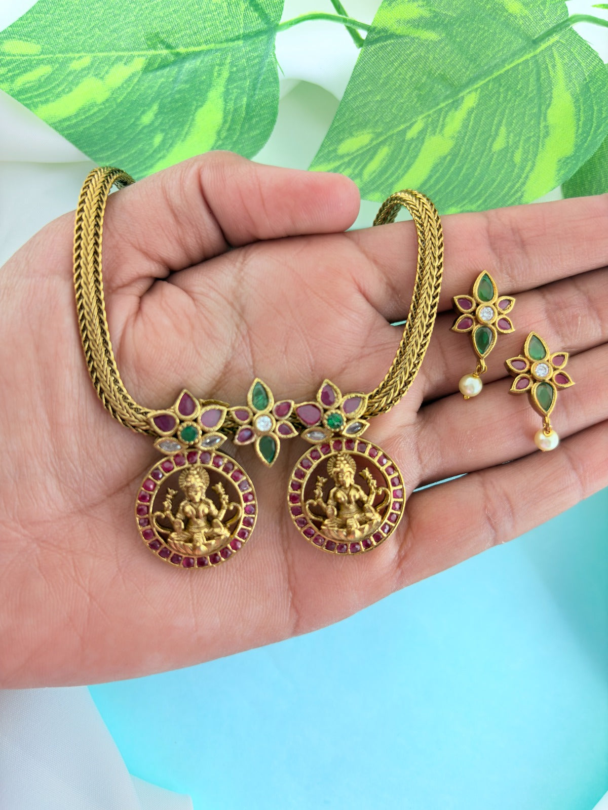 Premium antique finish necklace showcasing classic rich ruby and green stones with a lakshmi pendant and matching earrings