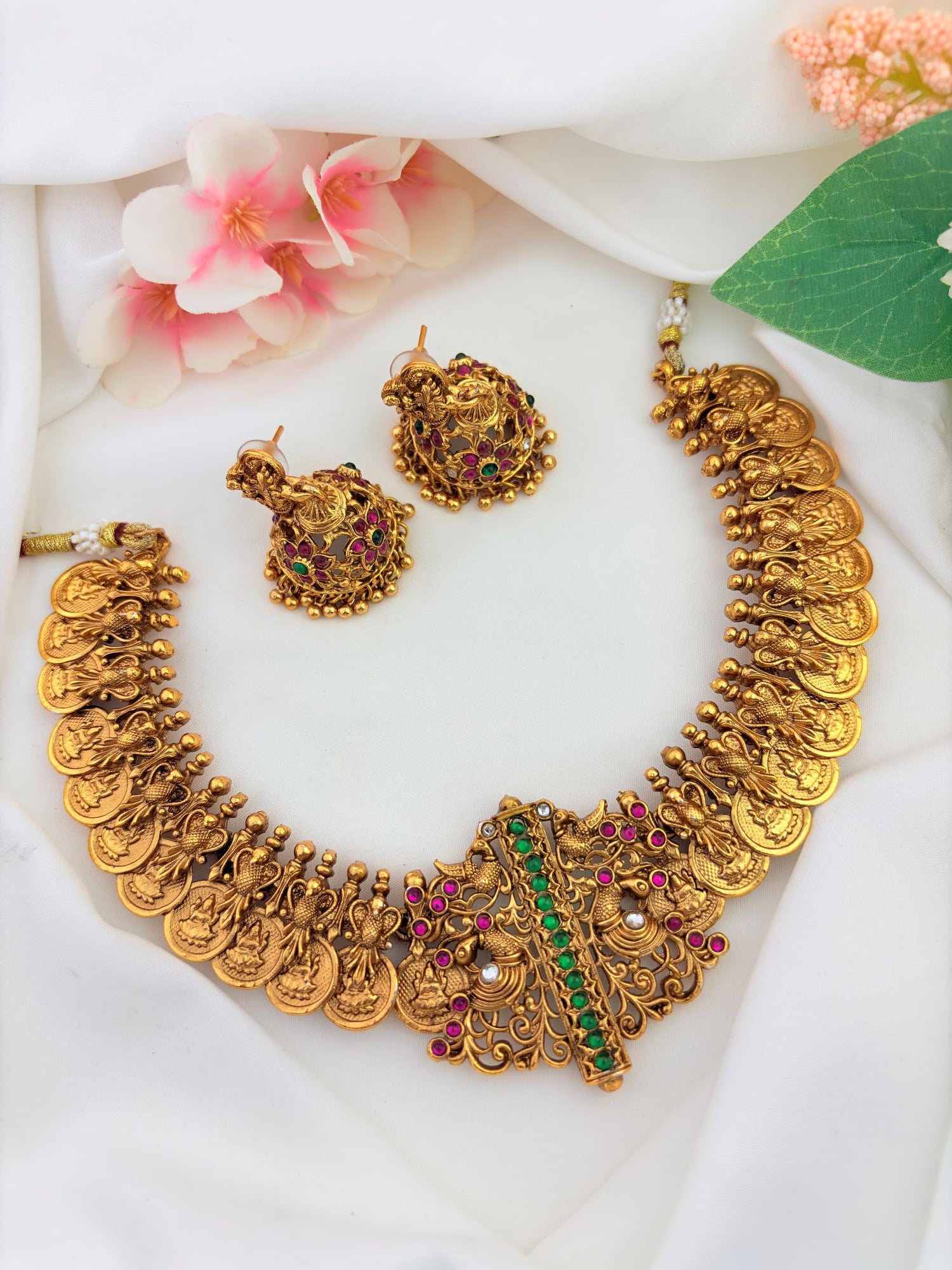 Traditional temple jewellery featuring intricate divine motifs, rich antique detailing, ruby and green stones